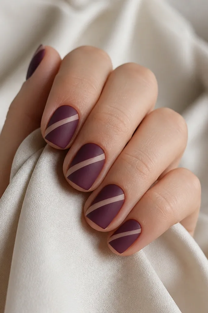 Short square nails painted matte plum-purple; each nail has a diagonal nude stripe running from cuticle toward one side, matte finish.