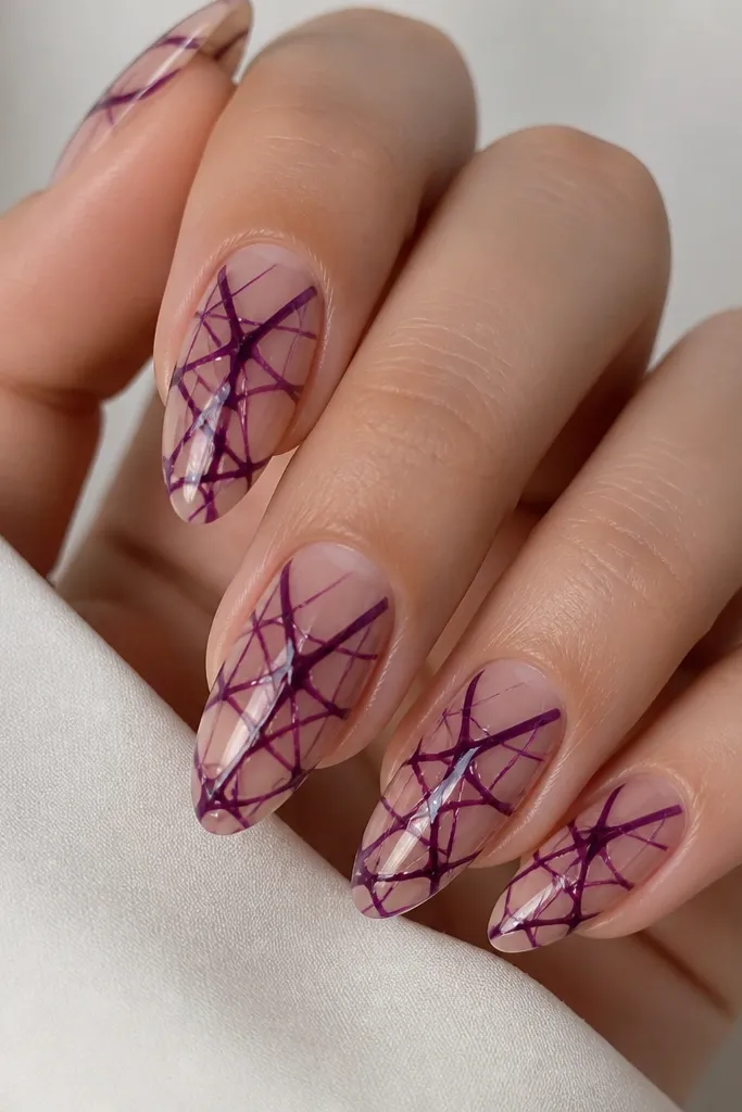 Clear nude nails with a glossy finish; dark purple web lines crisscross over the center, with small negative-space gaps, no glitter.
