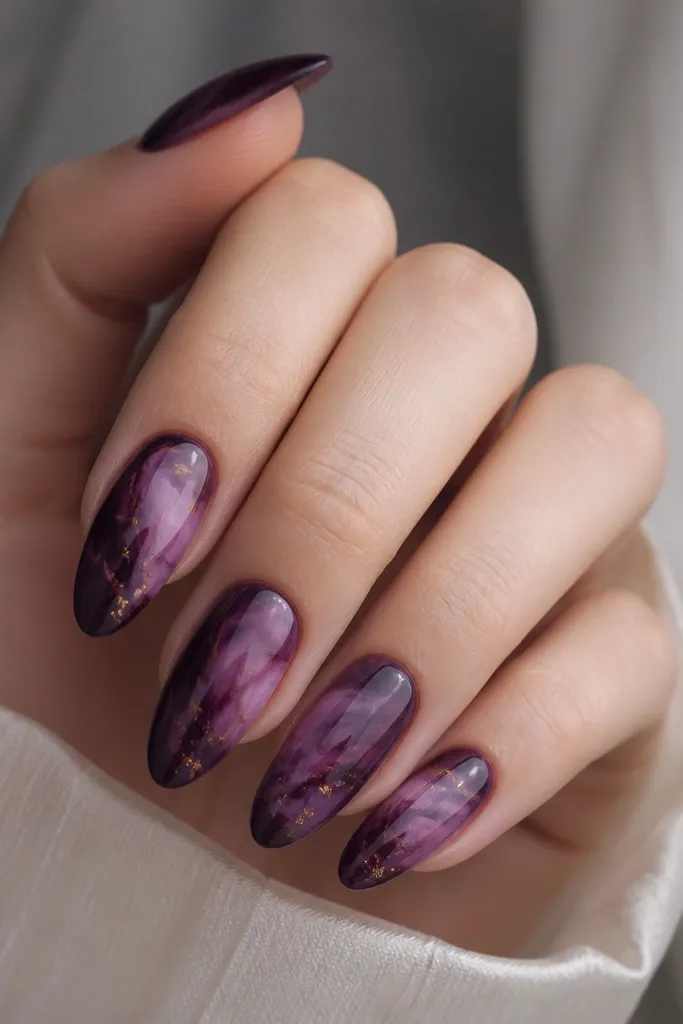 Almond nails with plum tie-dye swirls blending into a darker purple base; tiny gold flecks sprinkled near the swirls, glossy finish.