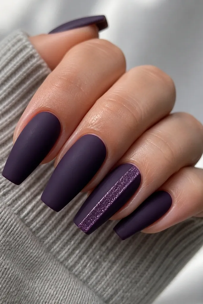 Medium coffin nails painted matte dark purple; one nail has a vertical glitter strip on the right side, like a satin ribbon, with matte on the rest.