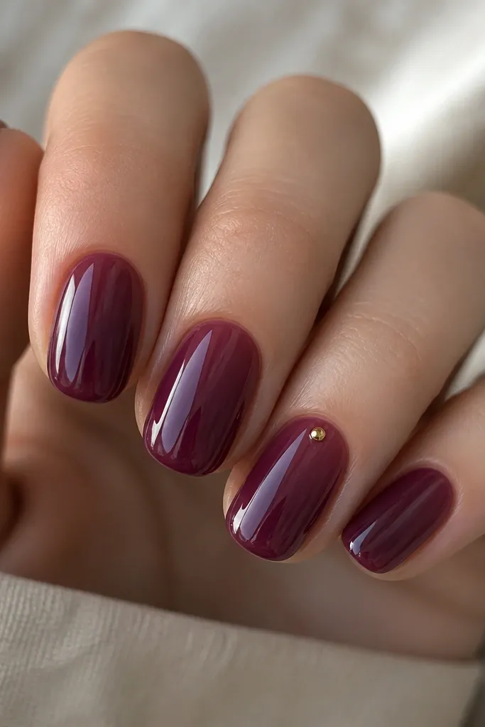 Glossy plum jelly nails. The color looks slightly translucent, with a juicy depth. One accent nail has a tiny gold dot near the cuticle.