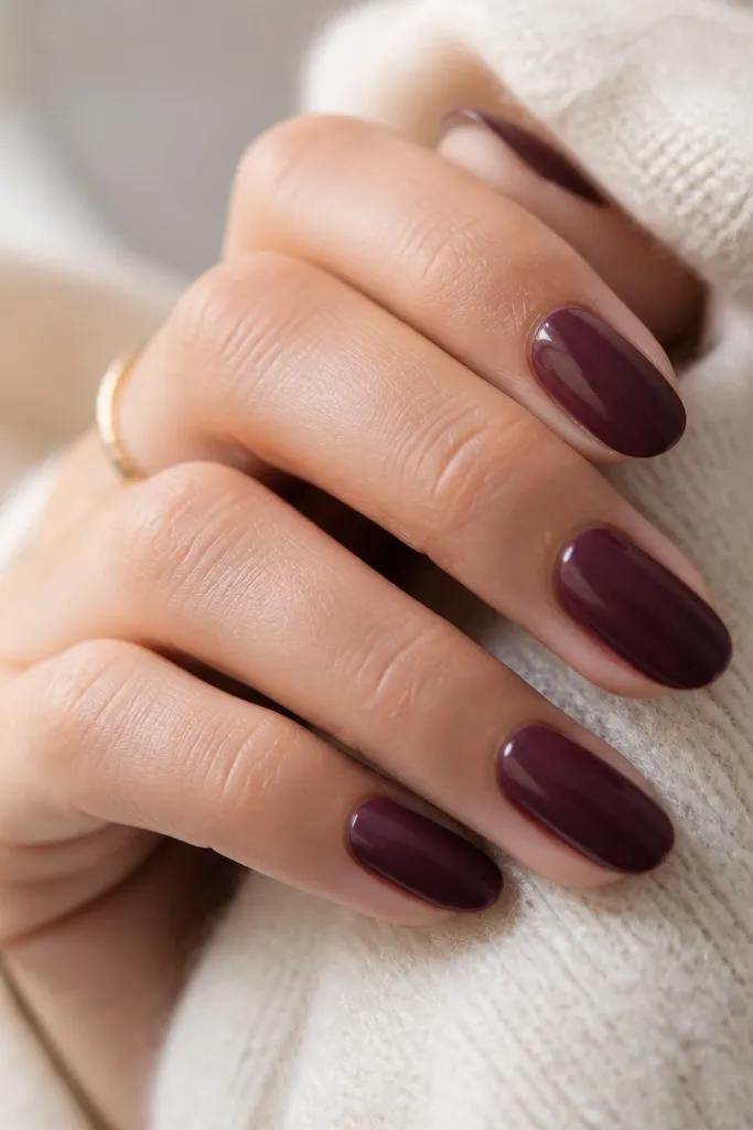 Short almond nails in a creamy plum-wine purple. The finish is glossy but not mirror-smooth, with a soft glow that catches light along the nail curve.