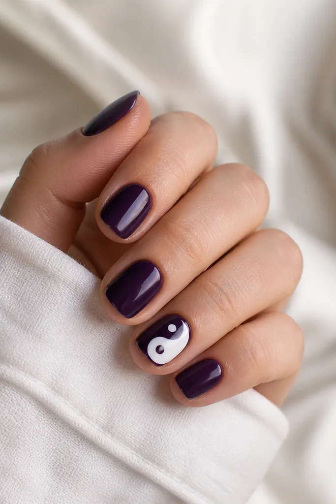 Short nails painted solid dark purple. On one accent nail, a tiny yin-yang symbol is painted in deep purple and white with a small dot detail.
