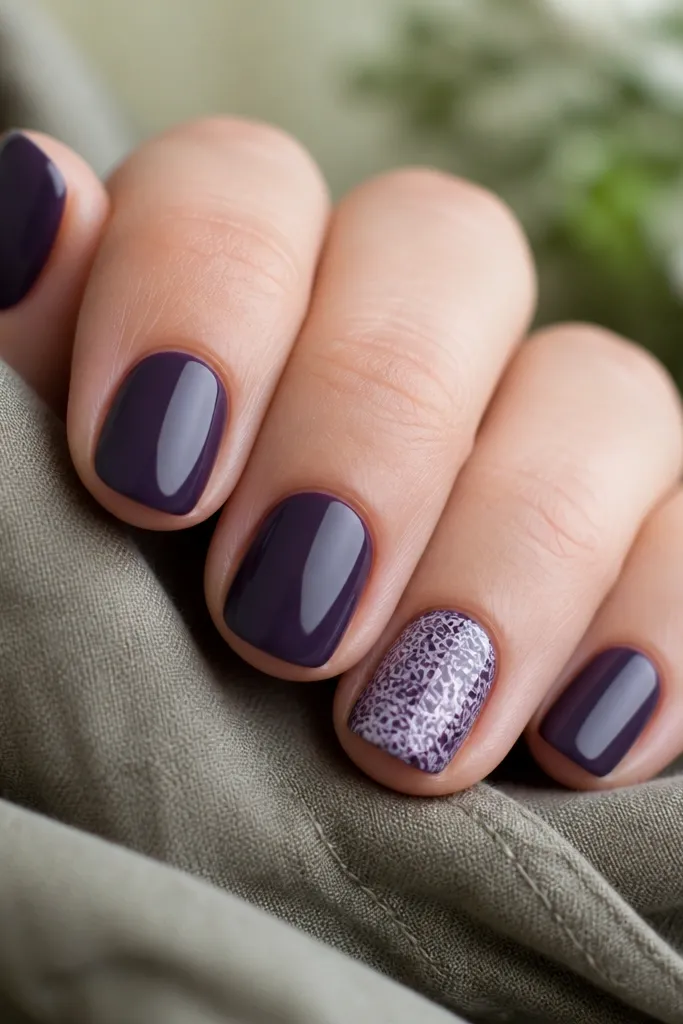 Short nails in solid dark purple. One nail has a delicate lace pattern in lighter purple and white, like a stamped doily effect, with crisp edges.