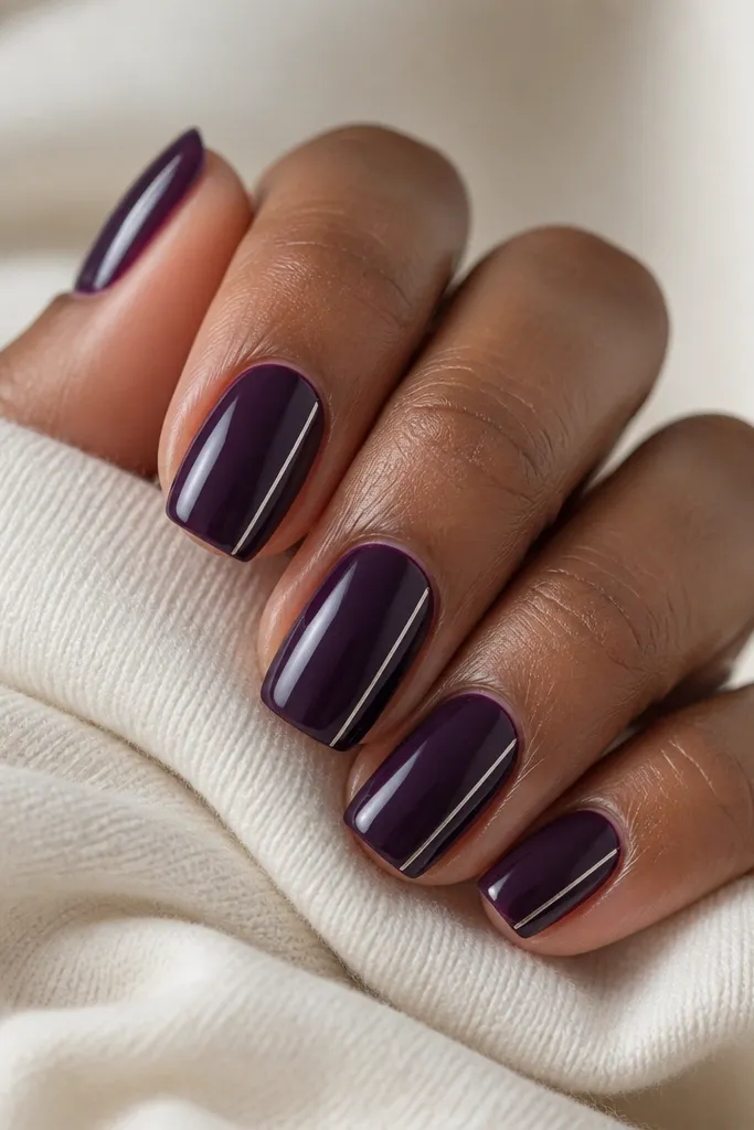 Short squoval nails painted solid dark purple. On each nail, a single thin silver line runs down one side of the nail, starting near the cuticle and stopping before the tip curve.