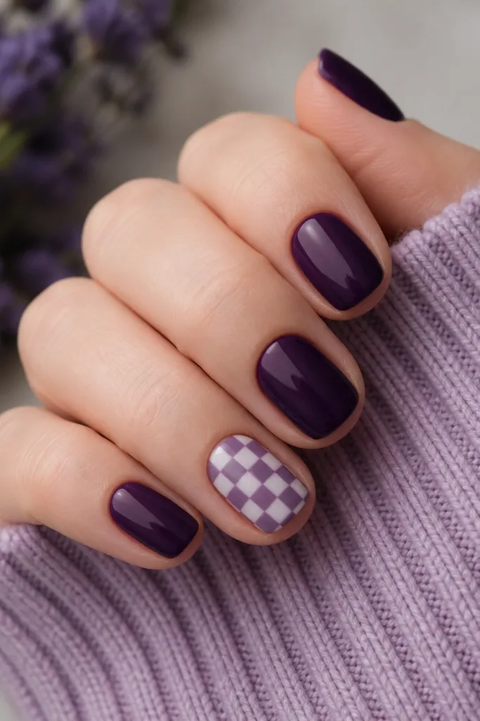 Short nails in solid dark purple. Two accent nails have a tiny checker pattern in lighter purple and white, with small squares that fit the nail width.