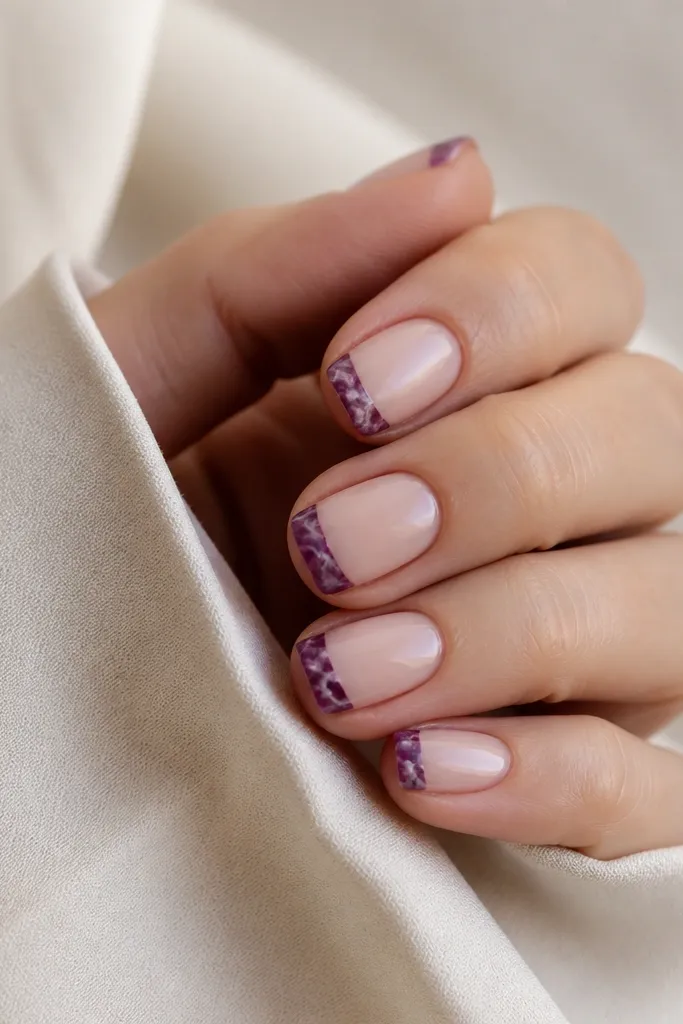 Short nails with a nude base. The tips are dark purple marbled with thin white veins, while the rest of the nail stays clean and nude.