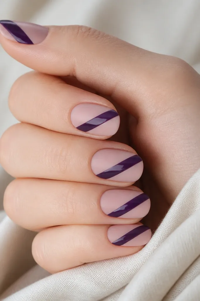 Nails painted nude-pink. On top, a diagonal dark purple tape line creates a clean slanted stripe. The stripe has a glossy finish while the rest is matte.
