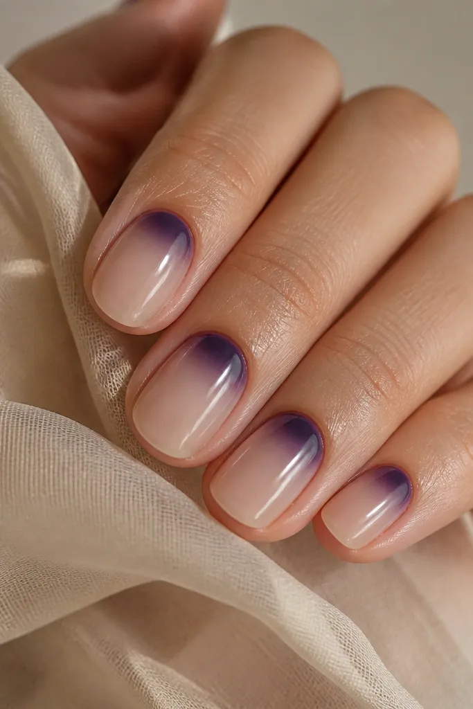 Nails with a nude base. A dark purple "halo" fades outward from the cuticle, forming a soft ring. The rest of the nail stays sheer and clean.