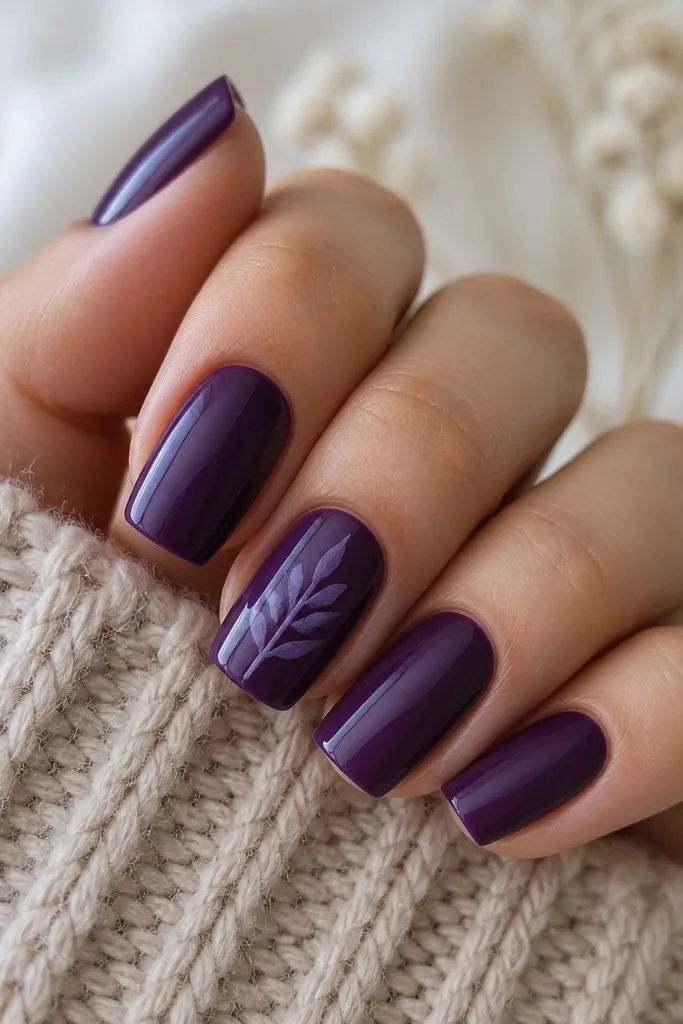 Deep purple solid nails with one accent nail featuring a simple leafy silhouette in lighter purple. A single thin vein line runs through the leaf.