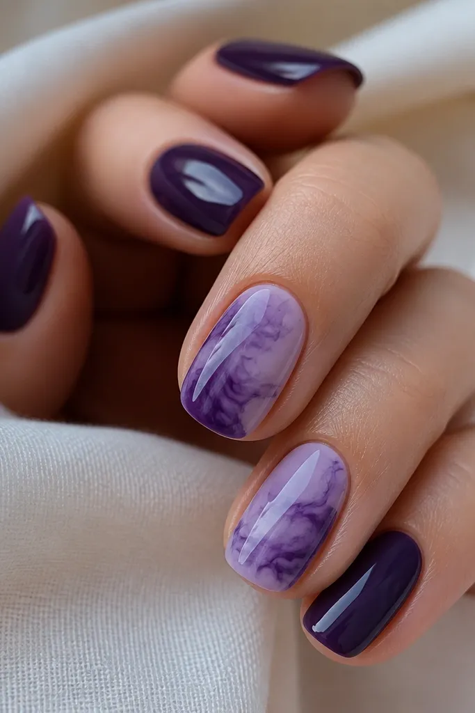 Glossy dark purple nails with a few swirly tie-dye bursts in lighter lavender on two nails. The swirls look like ink spread in water.