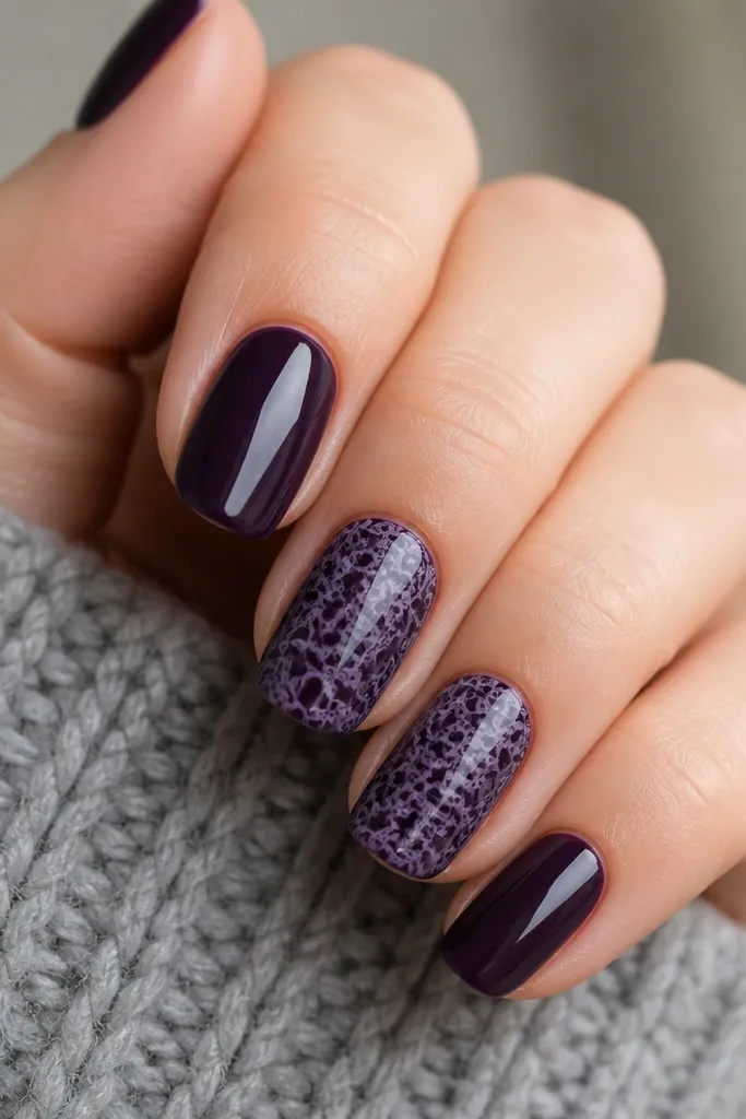 Glossy dark purple nails with a lace pattern stamped on two nails. The lace is lighter purple and looks like tiny repeating loops.
