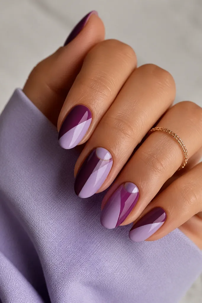 Diagonal design: one side of each nail is plum, the other is lilac, with a diagonal split. The split creates a half-moon shape near the cuticle on the accent nails.