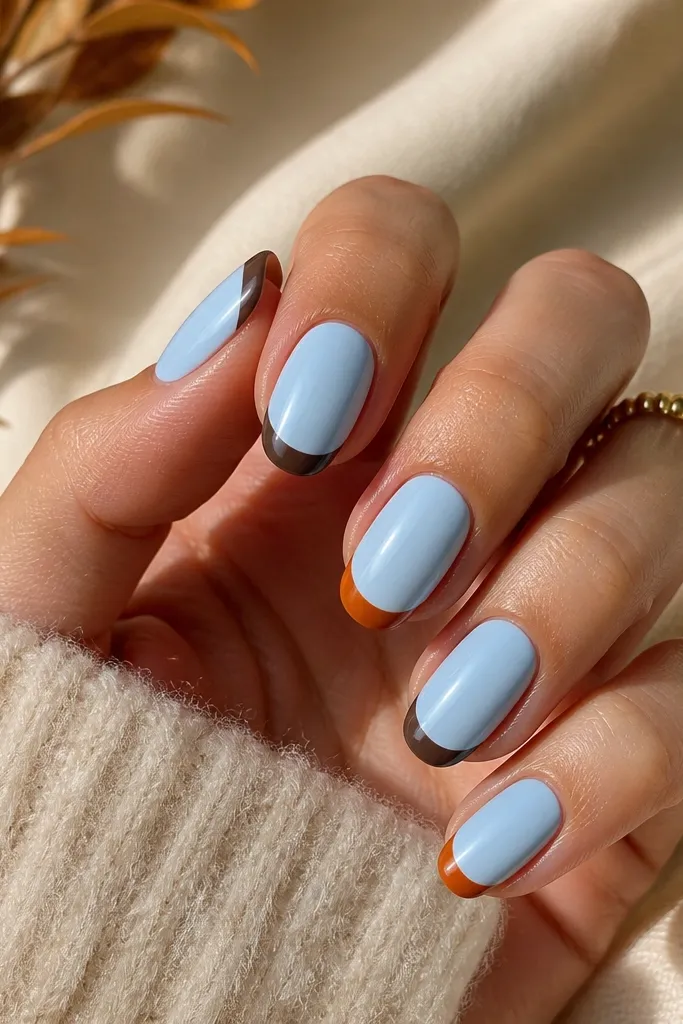 Nails have a powder blue base, glossy. The French tips are painted in a mix of autumn spice colors - burnt orange and chocolate brown - with a clean smile line on each nail.