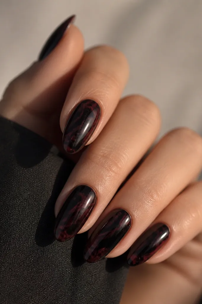 Dark nails with a black base. Oxblood marble swirls spread across each nail in thin, cloudy streaks. The overall look is glossy, with marbling that varies nail to nail.