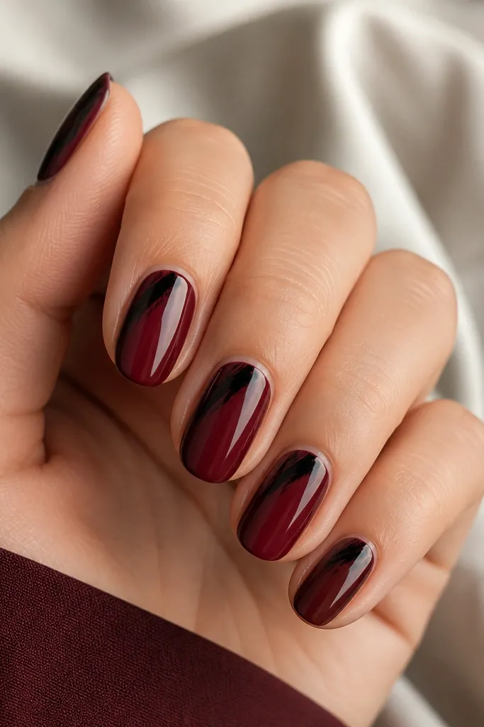 Oxblood glossy nails. Each nail has black brushstroke corners in the upper sides, like diagonal paint starting from the sides and stopping before the center. One nail has a bigger corner stroke.