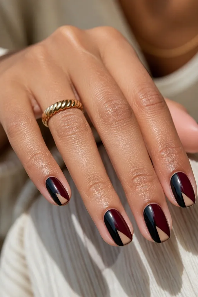 Each nail has a diagonal split: one side black, the other oxblood. In the center near the tip, a small negative-space triangle stays clear. The lines are sharp, and the finish is glossy.