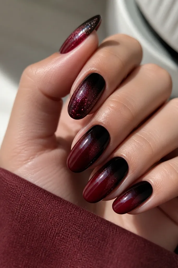 Nails have glossy black tips taking the top third. The transition into the red base is soft, and there's a micro glitter fade in oxblood tones near the border. One nail has extra glitter concentrated at the tip.