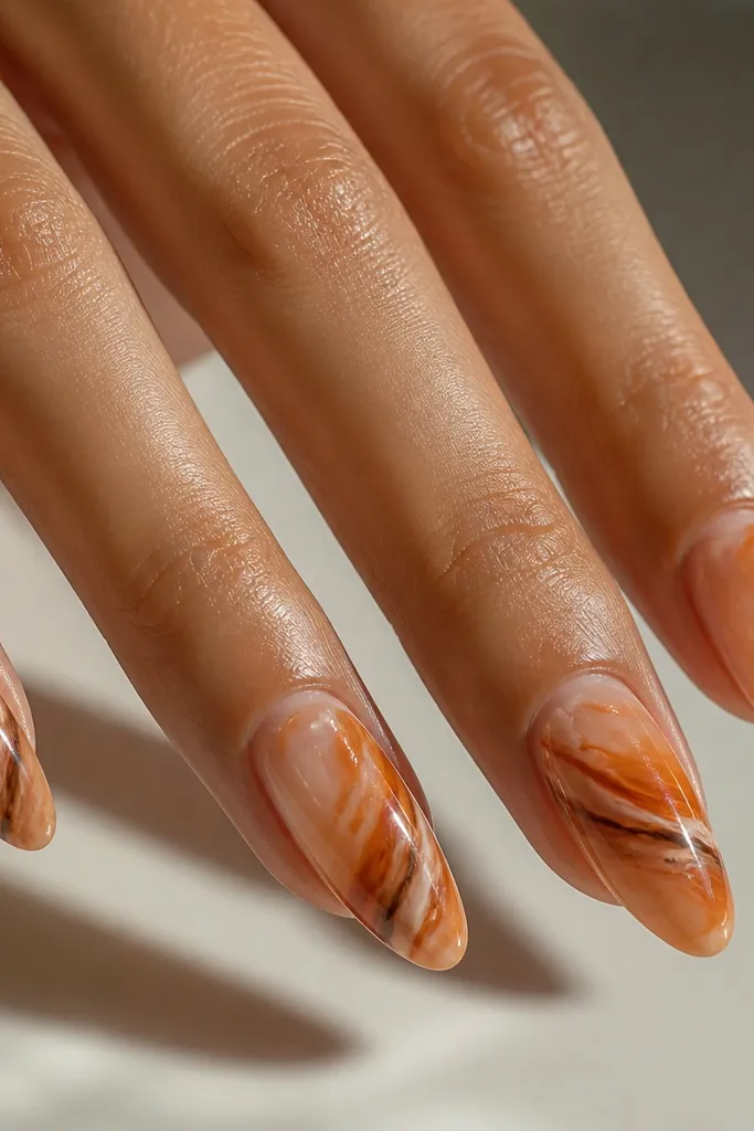 Medium almond nails on a nude base. Each nail has burnt orange marble swirls with thin streaks of chocolate brown and a few tiny white highlights. The swirls look like realistic stone, with glossy shine and no flat patches.