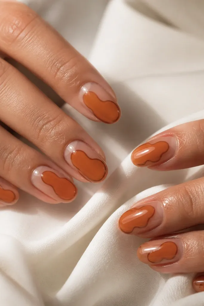 Medium oval nails with a clear jelly overlay. Beneath it, orange shapes appear like they're floating, and a thin brown outline frames the orange on each nail. The nails look glossy and slightly dimensional.