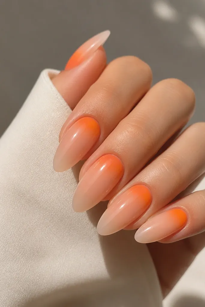 Long almond nails with a soft aura effect. The center near the cuticle glows in tangerine orange, fading outward into nude. The aura is strongest around the cuticle line. Glossy finish makes it look like a halo.