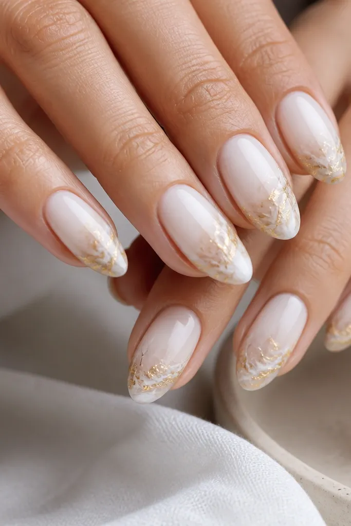 Milky white nails with marble swirls concentrated at the tips, and gold metallic swirl streaks running through the marble, glossy finish.