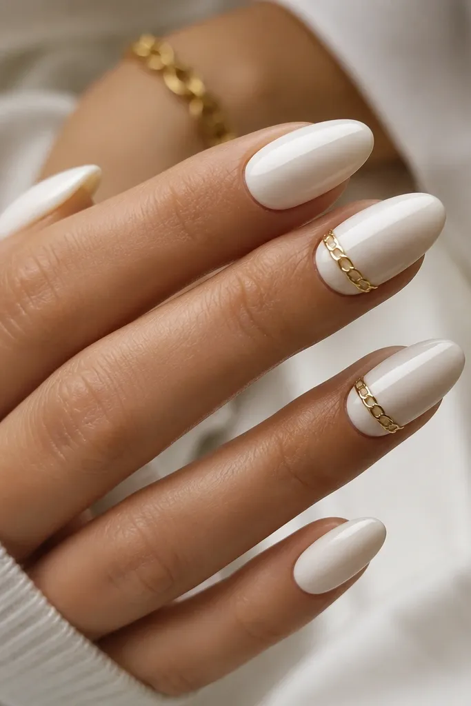 Medium almond nails with a solid glossy white base. On two nails, a tiny gold chain link design sits across the center - three to four small linked loops. The rest of the nails are plain white with a mirror shine.