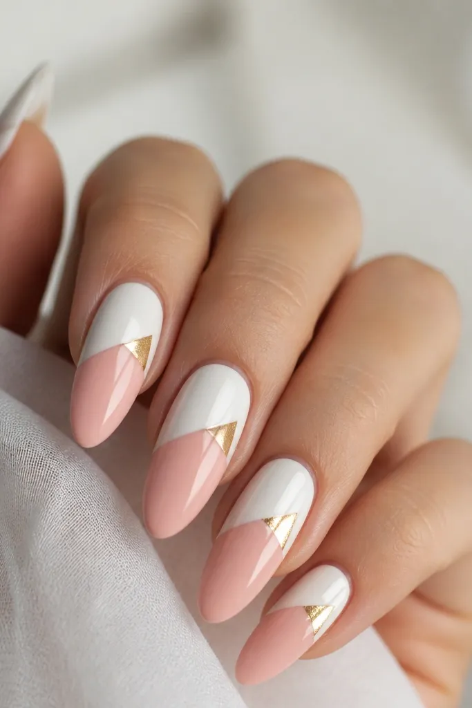 Long almond nails. The bottom half of each nail is blush pink, and the top half is opaque white. At the top corner where white meets pink, there's a small gold foil triangle. High shine top coat.