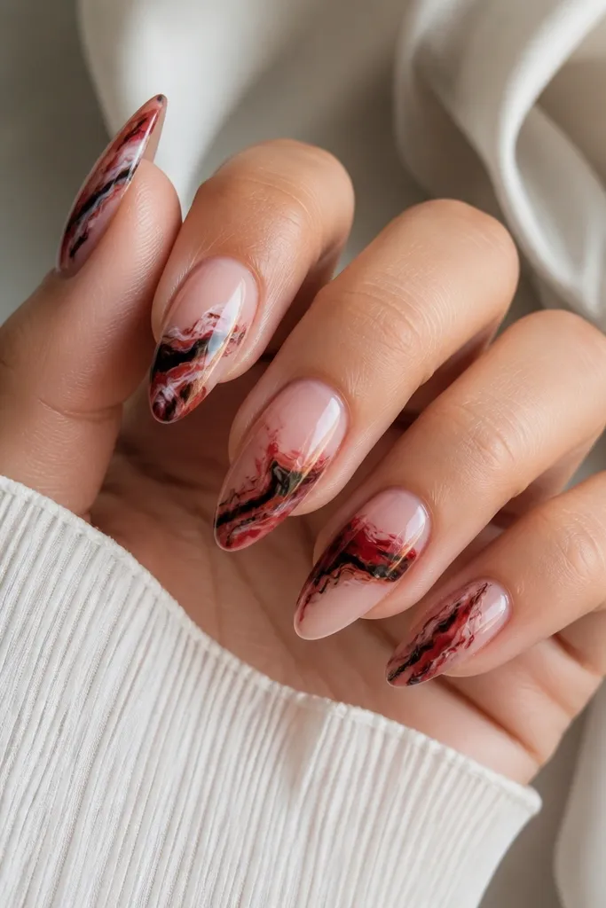 Each nail has a marbled pattern in red and black on a clear base, with thin white-ish swirls. The ring finger has a thicker marbled band across the middle.