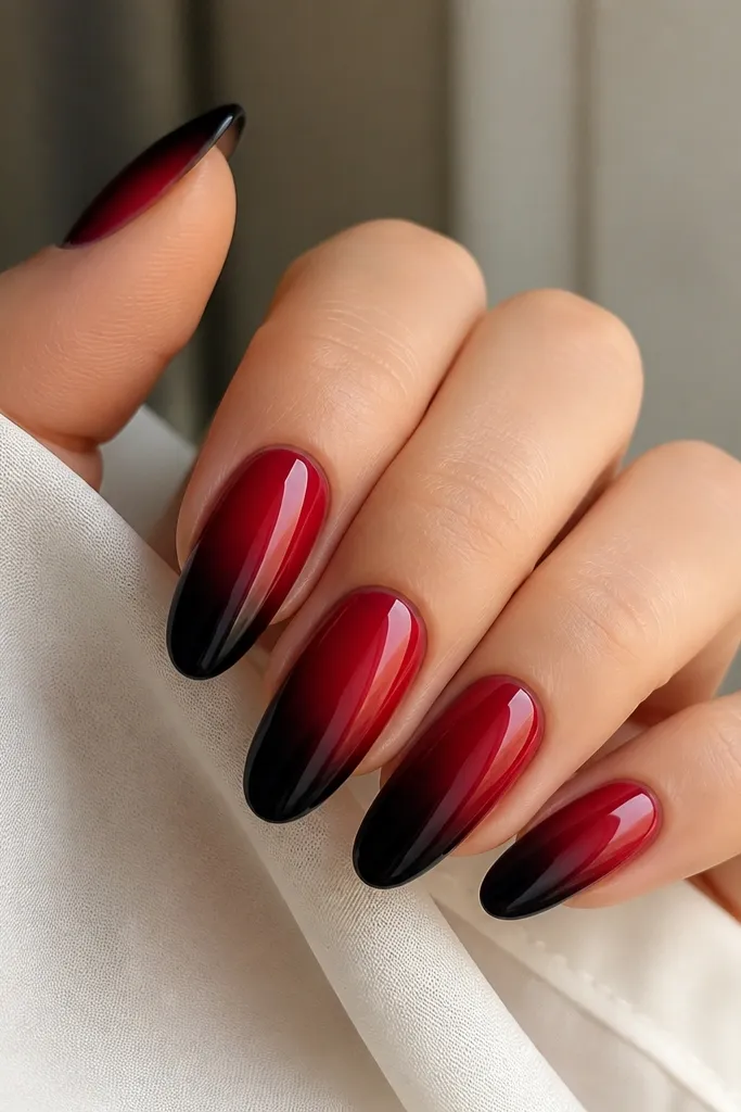 An ombre from black at the tip to deep cherry red toward the center, with the brightest red band in the middle. The nails look smooth and glossy.