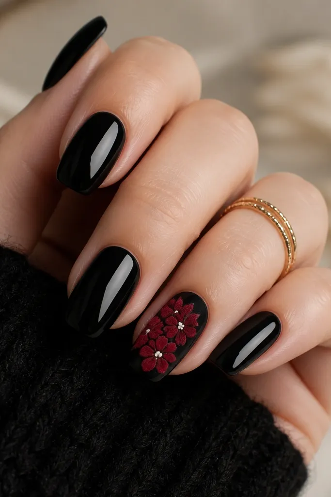 Four nails are glossy black. One nail is glossy black with a red velvet-looking stamped flower cluster centered, plus tiny white dot highlights.