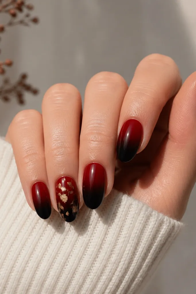 Nails show a smooth gradient: black at the very tip fading into crimson toward the cuticle. Gold foil sits like tiny confetti on the ring finger and a single corner on the thumb.