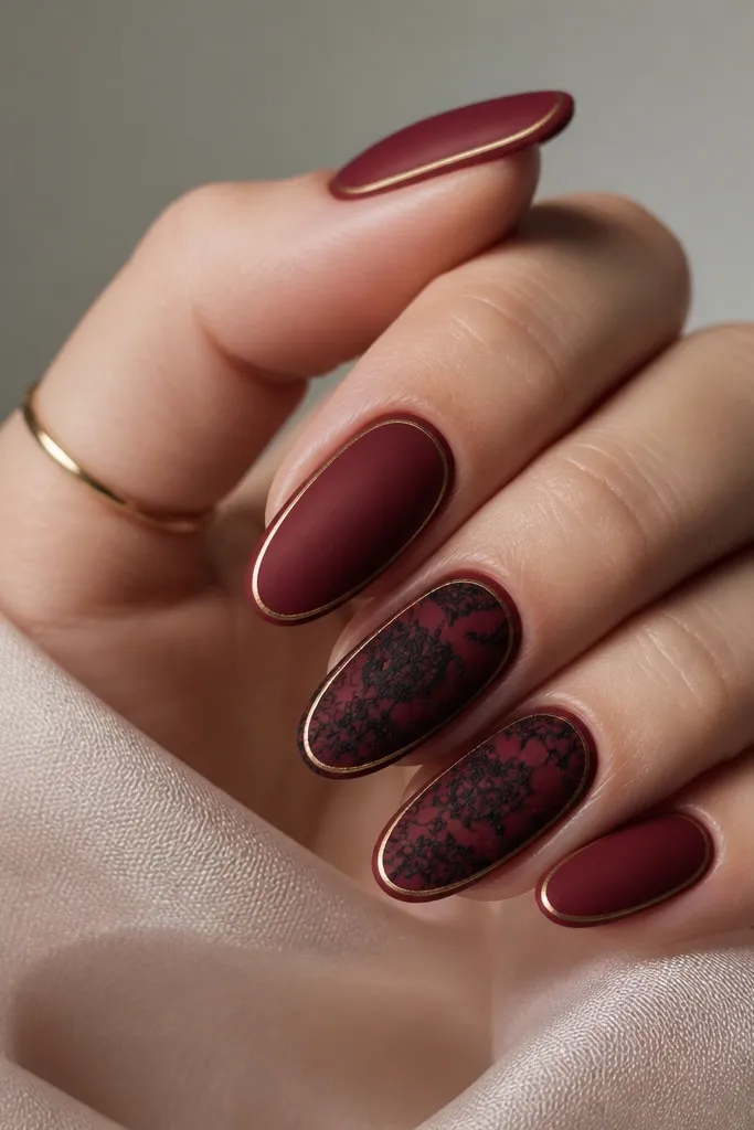 Nails are matte deep red. A black lace pattern is stamped on the middle and ring nails. The nails have a thin gold frame line near the outer edges, like a border.