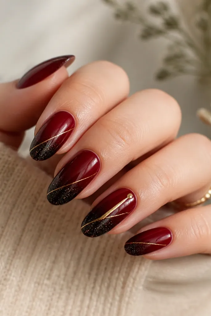 Nails have deep red base with a soft fade into black glitter at the tips. A thin gold thread line runs diagonally across each nail from lower left to upper right. Ring finger has a thicker gold line and a tiny gold dot near the tip.