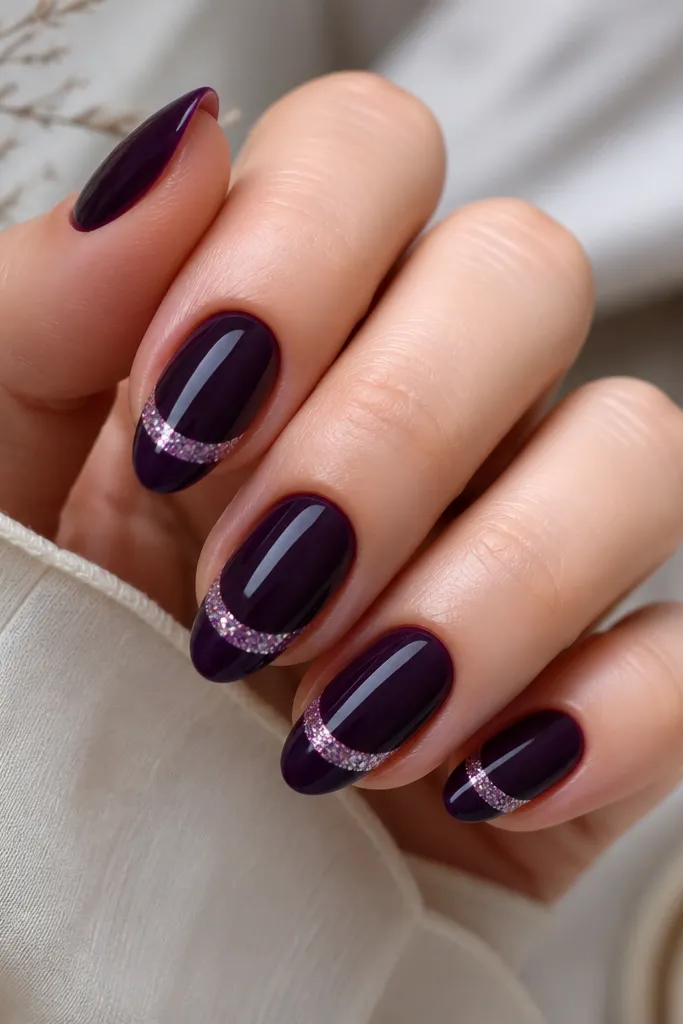 Medium almond nails with a dark purple base; French tips are painted deep purple too, and a chunky glitter "smile line" sits right above the tip edge, leaving a small clean border.