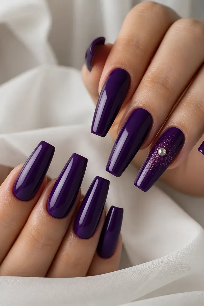 Long coffin nails with smooth deep purple base; one nail has a single small clear rhinestone near the center with a halo of fine glitter around it, glossy topcoat on the whole nail.