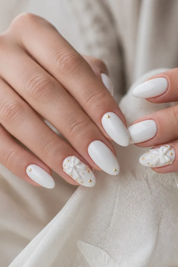 Medium almond nails in glossy white. On two accent nails, a tiny 3D white bow sits near the cuticle, and around the bow are small gold dot clusters. Other nails are plain white with a single gold dot near the tip.