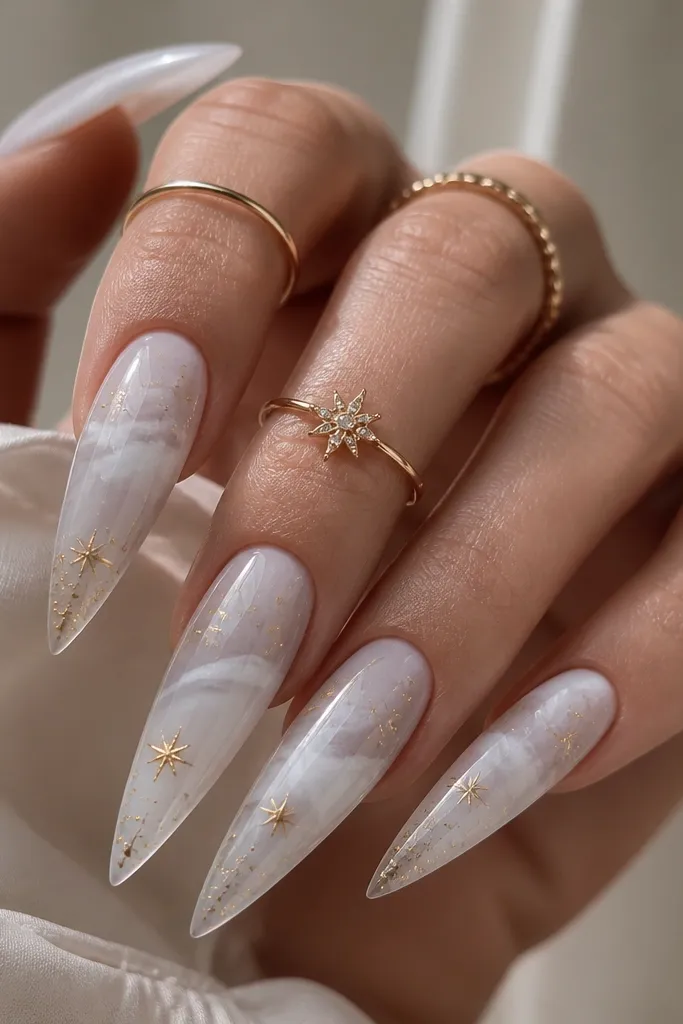 Long stiletto nails with a white galaxy swirl - soft gray-white clouding with a milky base. Gold star specks and tiny gold dots are scattered, mostly toward the tips. High gloss top coat.