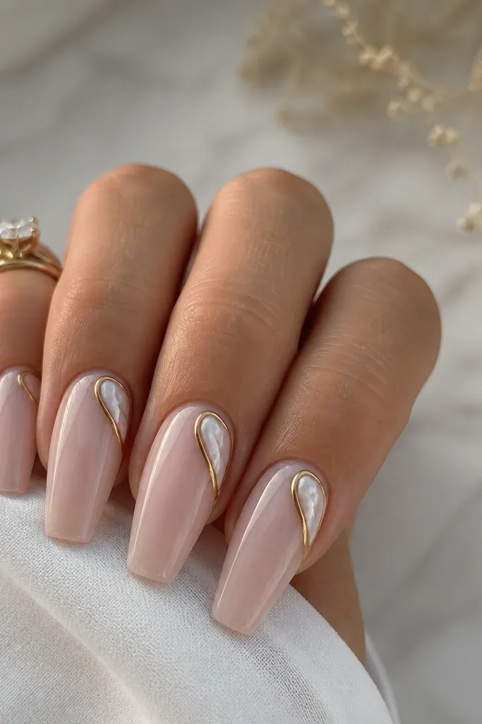 Coffin nails with a glossy sheer nude base. Each nail has a pearl white swirl tucked into the top corner near the sidewall, outlined with a thin gold line. Gold is only around the swirl, not across the whole nail.
