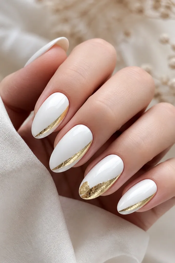 Five nails: four have glossy white with a single diagonal side-swoosh in gold foil starting near the sidewall mid-nail. One accent nail is fully white with a larger gold foil patch near the tip.