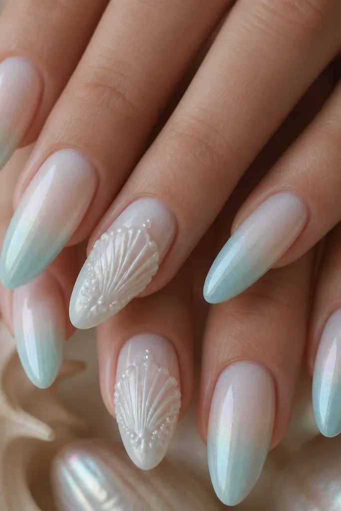 Long almond nails painted milky pearl white with a seafoam fade at the tips. Two accent nails have raised icy white seashells with tiny pearl beads along the shell ridges, plus a subtle holographic shimmer in the background.
