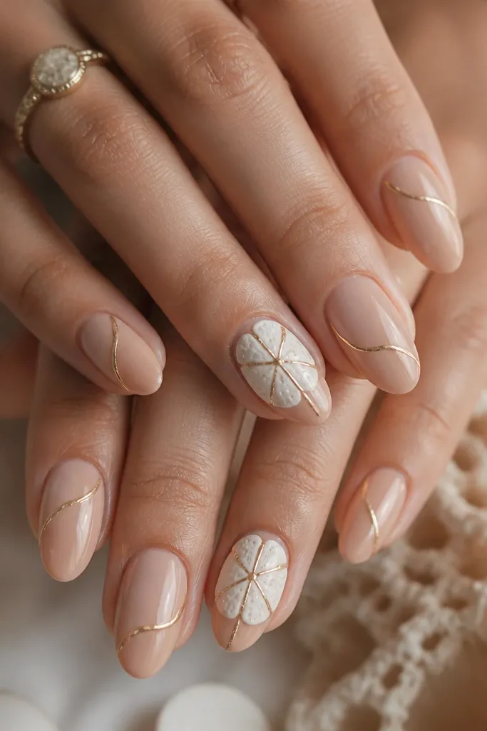 Medium almond nails painted warm nude. Accent nails have raised sand dollar shells in off-white with tiny gold line art radiating from the center. The rest of the nails have thin gold wave lines.