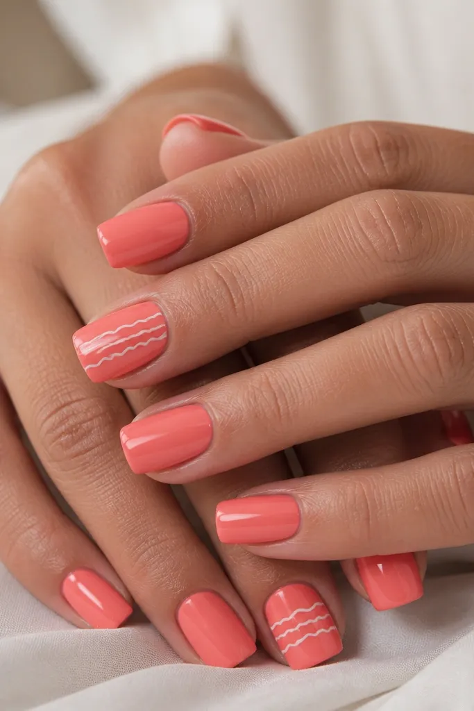 Square nails in coral pink. White squiggle lines run horizontally across the center of two nails, with the rest solid coral and glossy finish.