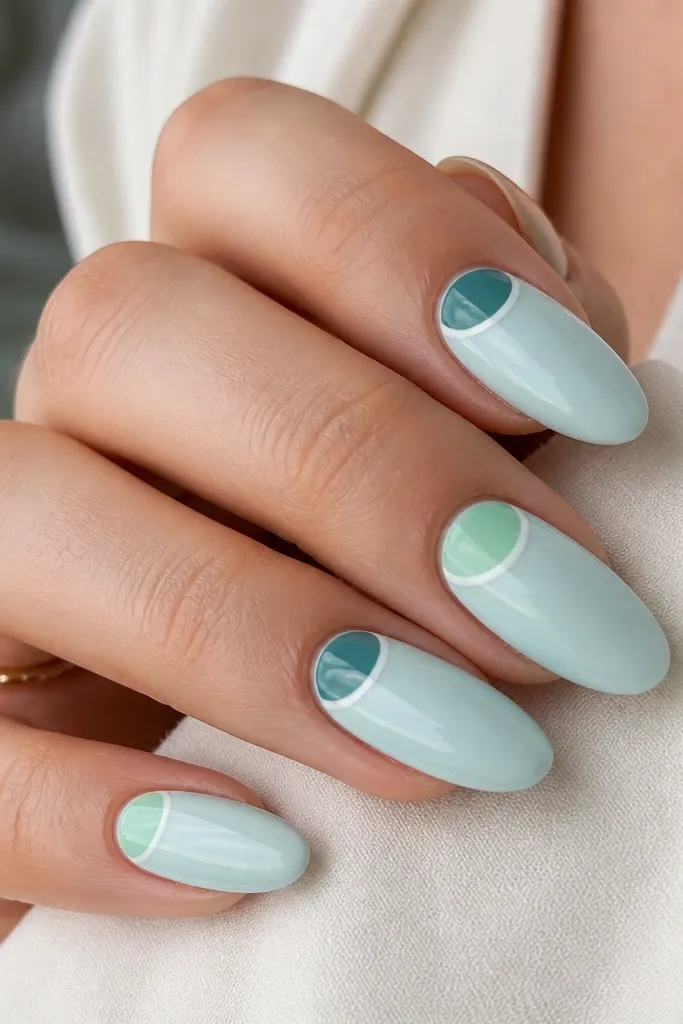Almond nails with a pale milky aqua base; half-moon shapes near the cuticle in mint green and translucent teal, outlined with a thin white line on alternating nails.