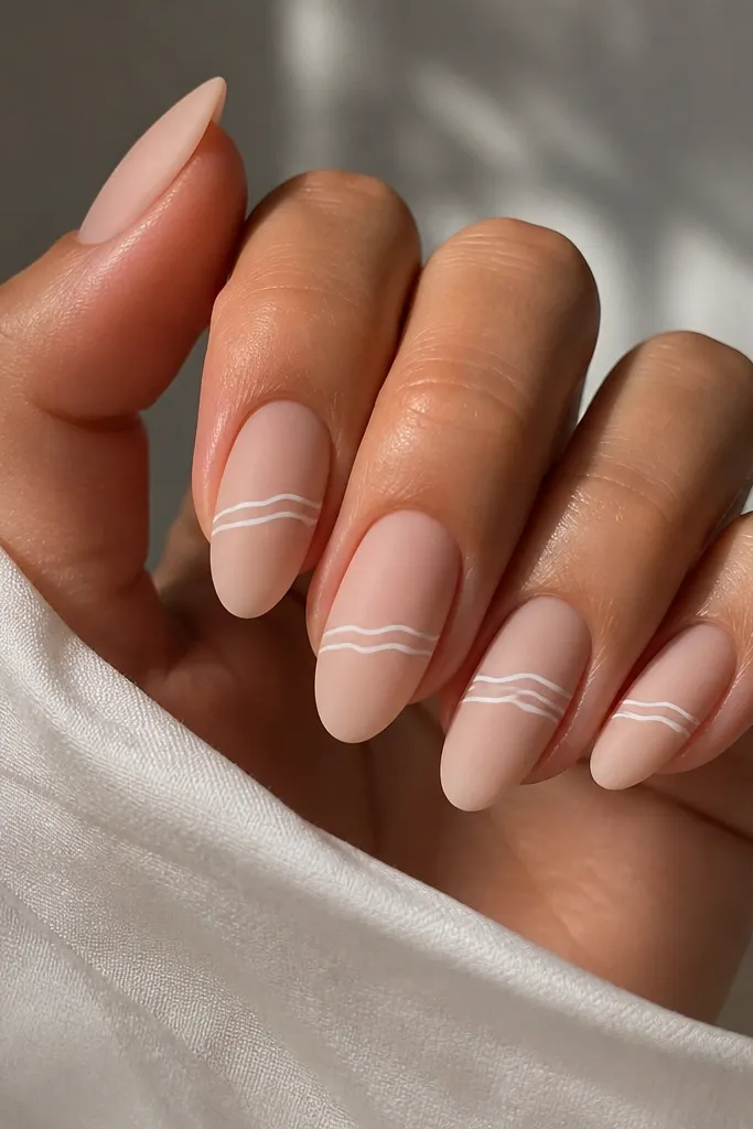 Nude almond nails with a matte or satin finish; thin white wavy lines run horizontally across the middle third, with one nail having two extra waves.