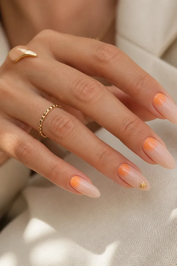 Almond nails with a nude base; a soft orange gradient wash sits just around the cuticle area like a glow, fading outward; one nail has a tiny gold star near the tip.
