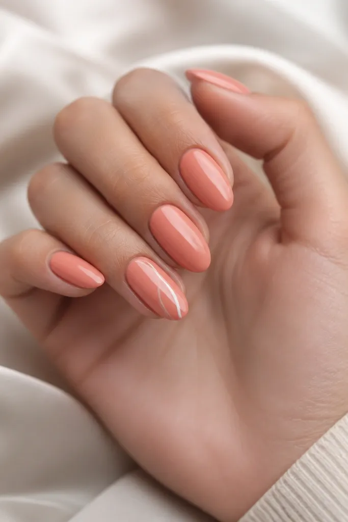 Almond nails in coral cream glossy polish, with a single accent nail featuring a thin white swirl from mid-nail toward the tip.