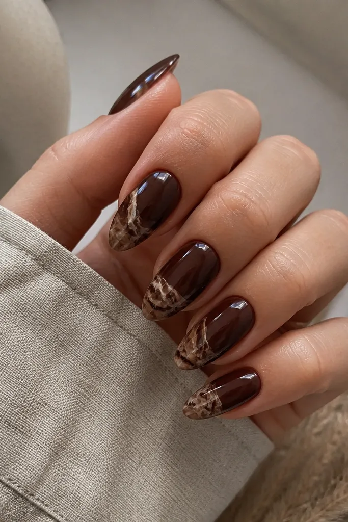Almond nails with glossy espresso brown base and nude marble veining concentrated on the tips, finished glossy.