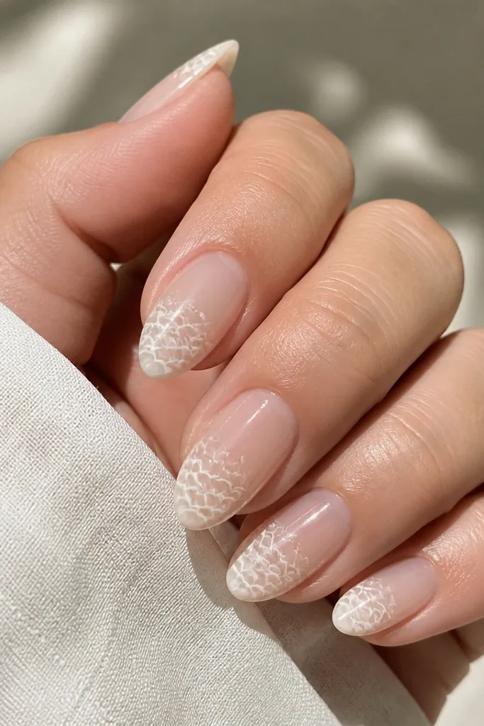 Almond nails in champagne nude. The tips have a frothy sea-foam pattern: tiny scallops and short curved lines in pearly white, fading into the nude toward the cuticle.