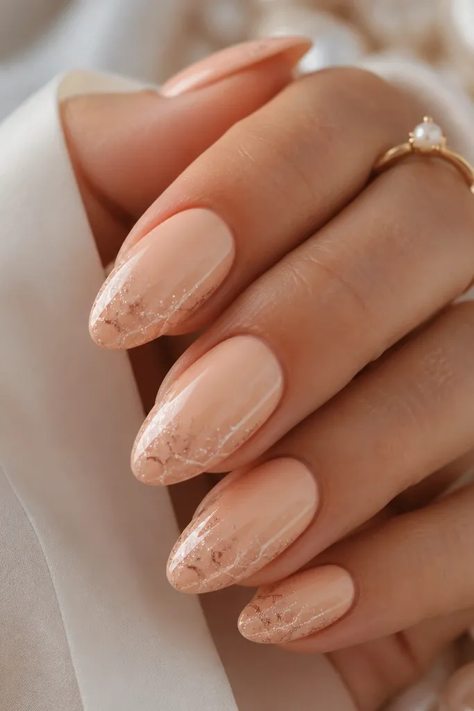 Soft peach almond nails. The shell design is made of tiny arcs and micro specks in rose-gold shimmer, concentrated near the outer edge, with a creamy glossy finish.